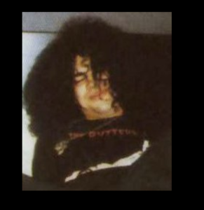 Drunk looking Slash wearing a Guttersluts t-shirt while laying down on a bed, cigarette in his mouth. 